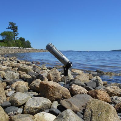 WERU.org website background, a mic nestled in ocean rocks with the ocean behind it